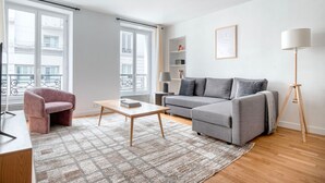 Een moderne woonkamer met een grijze bank, een roze fauteuil, een houten salontafel en een vloerlamp.