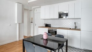 Een moderne keuken met witte kastjes, een magnetron en een spoelbak. Er staat een glazen tafel met twee stoelen en een roze vaas.