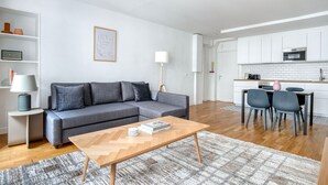 Een moderne woonkamer met een grijze bank, een houten salontafel en een eethoek met twee stoelen.