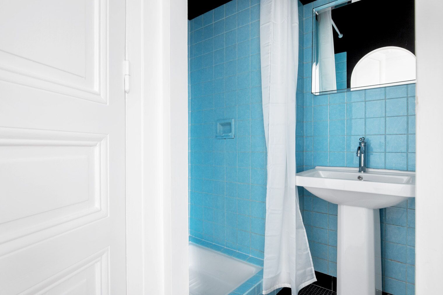Un bagno con piastrelle blu, un lavandino bianco e una porta bianca.