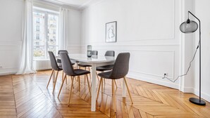 Un coin repas avec une table et des chaises blanches, un luminaire suspendu et un radiateur.