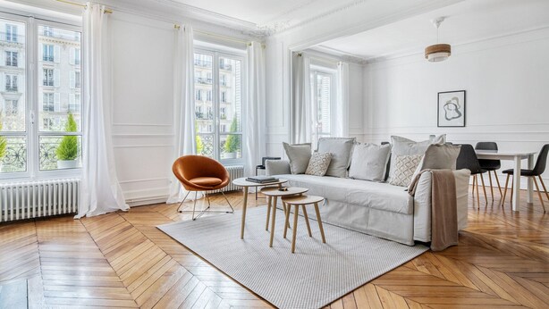 Un salon spacieux doté d’une grande fenêtre, d’un canapé, d’un fauteuil et d’un coin repas.