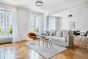 A spacious living room with a large window, a sofa, a chair, and a dining area.