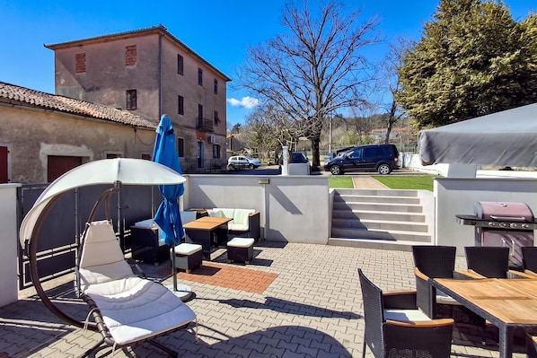 An outdoor patio area with a swing chair, tables, and a barbecue grill.