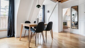 Ein Essbereich mit Holztisch und Stühlen, einer hängenden Pendelleuchte und Blick in die Küche durch eine offene Tür.