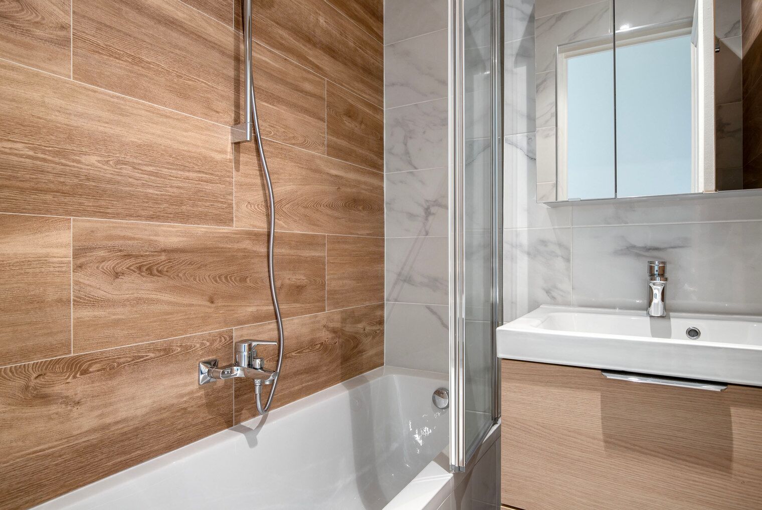 Une salle de bain moderne avec un plancher en bois, une douche en verre et un lavabo blanc doté d’un comptoir en marbre.