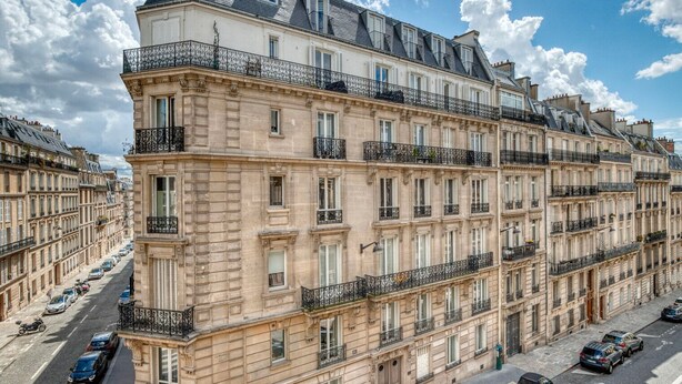 Un edificio a più piani con balconi, vista sulla strada e auto parcheggiate.