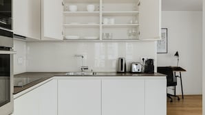 A modern kitchen with white cabinetry, a stainless steel sink, and a countertop with a toaster and kettle. - Blueground | Sentier-Montorgueil, foodie area (Paris)