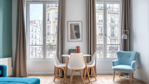Ein modernes Wohnzimmer mit Essbereich, großen Fenstern und Blick auf die Stadt, sowie einem blauen Sessel.