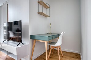 Relax in a clean and functional room with a flat-screen TV, desk, and wall-mounted shelf.