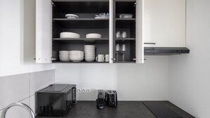 Eine moderne Küche mit einer eingebauten Mikrowelle, einem Toaster und einer Kaffeemaschine auf der Arbeitsfläche, darüber ein Schrank mit Tellern, Schüsseln und Gläsern.