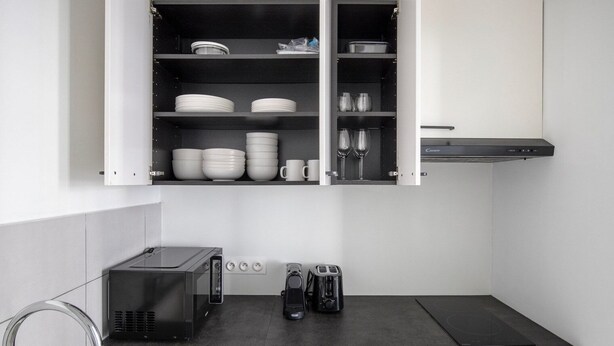 Eine moderne Küche mit einer eingebauten Mikrowelle, einem Toaster und einer Kaffeemaschine auf der Arbeitsfläche, darüber ein Schrank mit Tellern, Schüsseln und Gläsern.