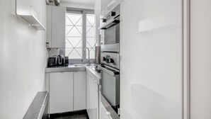 A compact kitchen with white cabinets, a built-in oven, and a window with cross ventilation. - Blueground | Europe, nr Gare Saint Lazare (Paris)