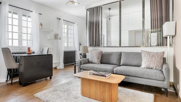 A modern living room with a grey sofa, a wooden coffee table, and a dining area with a dark table and chairs. - Blueground | Europe, nr Gare Saint Lazare (Paris)