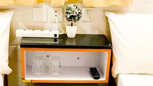 A compact refrigerator with a control panel, a small shelf with glasses and a remote control, and a potted plant on the countertop. - New World Guest House (Kowloon)