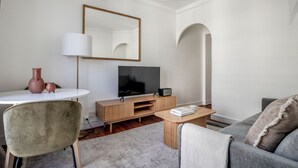 A modern living room with a television, a wooden entertainment unit, a round white table, and a grey sofa.