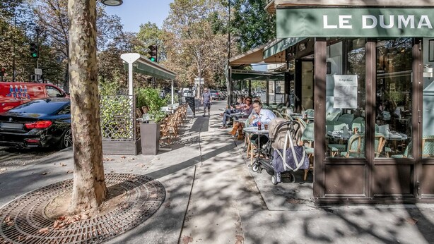 A café with outdoor seating, a tree, and a parked car.