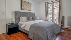 A bedroom with a bed, nightstand, and a window with curtains.