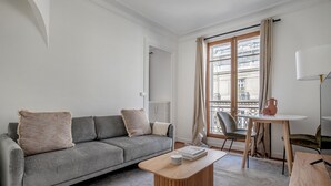 A modern living room with a grey sofa, a wooden coffee table, and a small round table with a vase.
