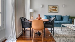 A modern living room with a round table, two black wicker chairs, a blue sofa, and a patterned rug.