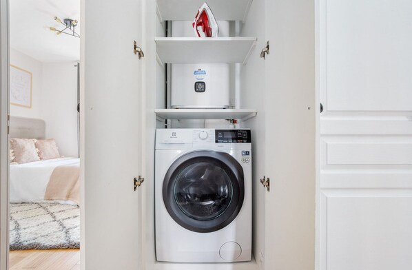 Une petite buanderie blanche, équipée d’un lave-linge à chargement frontal et d’un petit sèche-linge.