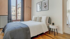 Una habitación de hotel con una cama grande, una mesita redonda y un ventanal con cortinas.