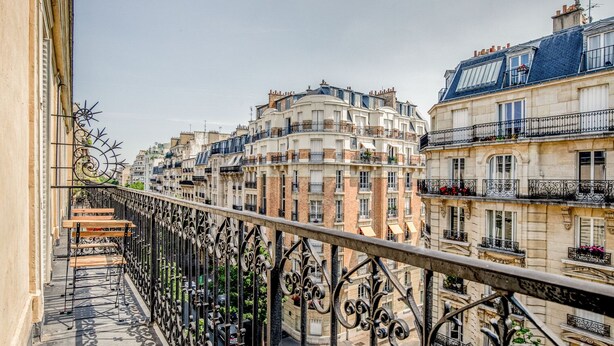 Un balcón con barandillas de hierro forjado ornamentadas que da a una hilera de edificios europeos clásicos con varios pisos y balcones.