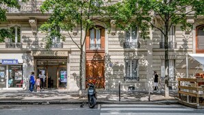Vista de una calle con un edificio de estilo arquitectónico clásico, una motocicleta estacionada y un paso de peatones.