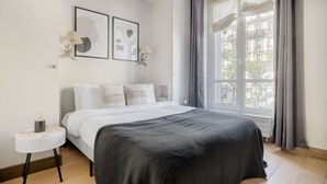Une chambre moderne avec un grand lit, une petite table de chevet et une fenêtre avec des rideaux.