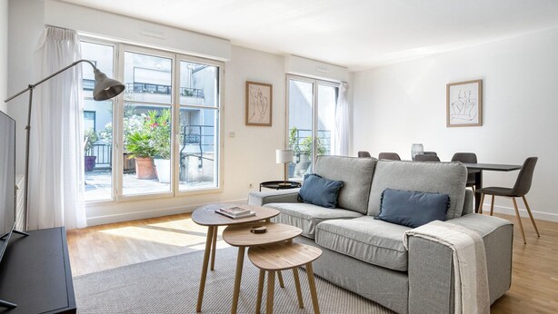Ein modernes Wohnzimmer mit einem grauen Sofa, einem kleinen runden Tisch und einem Essbereich mit Stühlen.