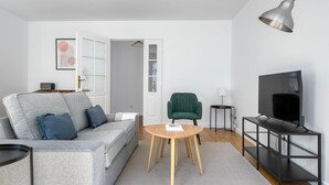 Ein modernes Wohnzimmer mit grauem Sofa, grünem Sessel, rundem Holztisch, schwarzem TV-Schrank und einer Pendelleuchte.