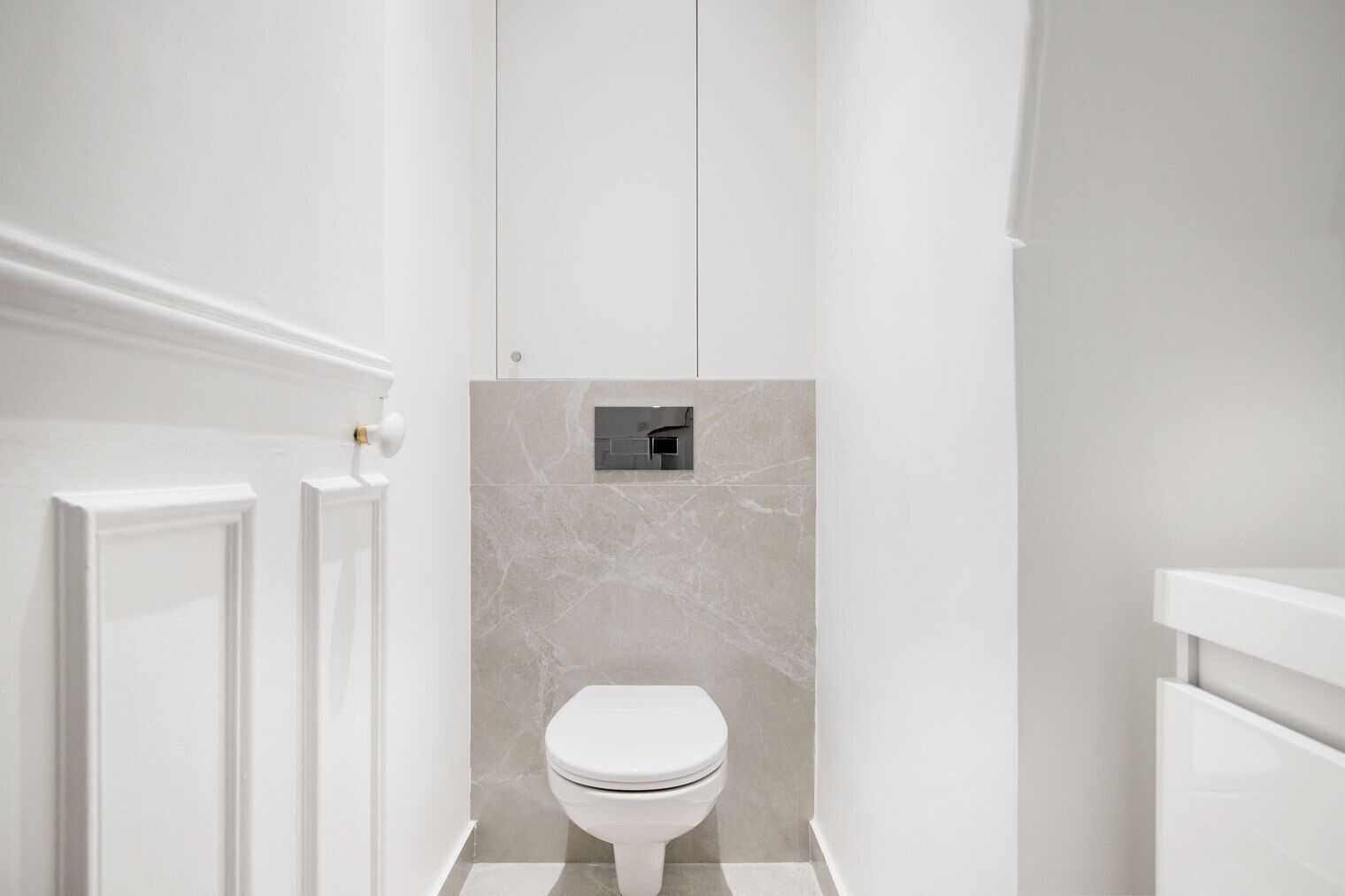 A modern bathroom with a toilet, a marble wall, and a white door.