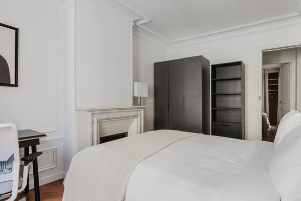 A bedroom with a bed, a desk, a chair, a wardrobe, and a fireplace.