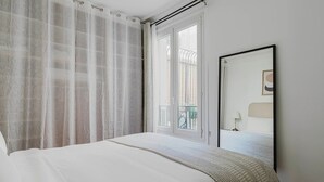 Een slaapkamer met een groot bed, een raam met uitzicht op een balkon en een ingelijst schilderij aan de muur.