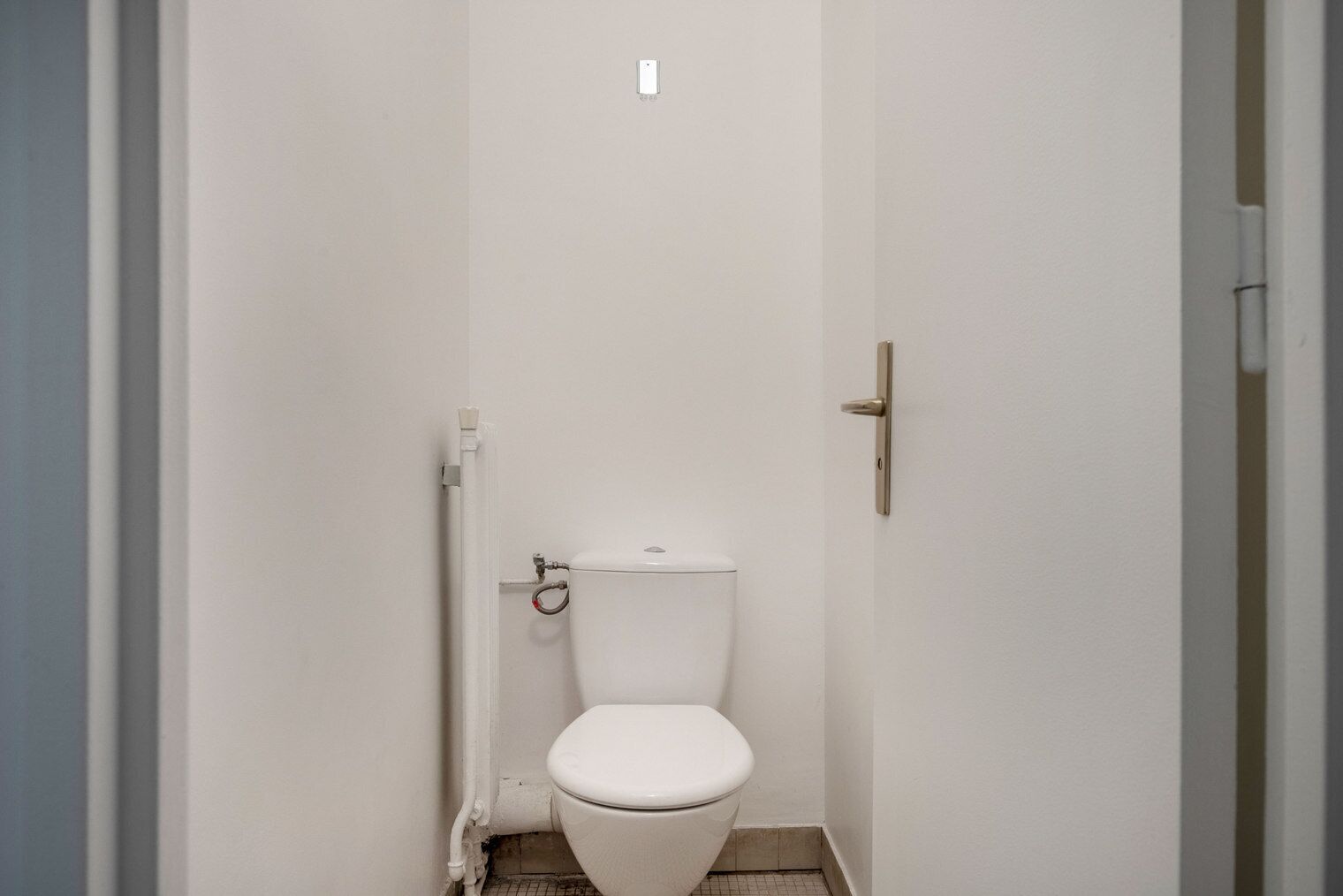 Une petite salle de bain blanche, conçue pour une seule personne, comprenant des toilettes, une chasse d’eau et une porte dotée d’une poignée dorée.