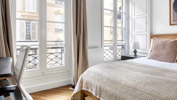 Une chambre d’hôtel avec un grand lit, une table de chevet, une lampe et une vue sur la ville grâce à de grandes fenêtres.