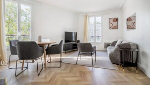 A modern living room with a dining area, a sofa, a TV, and large windows. - Blueground | Beaugrenelle, nr Seine & mall (Paris)