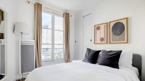 A hotel room with a large bed, a standing heater, a window with curtains, and two framed artworks on the wall. - Blueground | Beaugrenelle, nr Seine & mall (Paris)