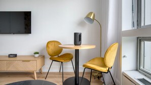 Un salon moderne avec une table ronde en bois, deux chaises jaunes, un lampadaire, un téléviseur et une petite plante posée sur un meuble en bois.