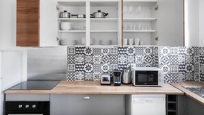 A compact kitchen with a wooden countertop, a built-in microwave, a kettle, and a dishwasher. - Blueground | La Muette, elev & balcony, nr mall (Paris)
