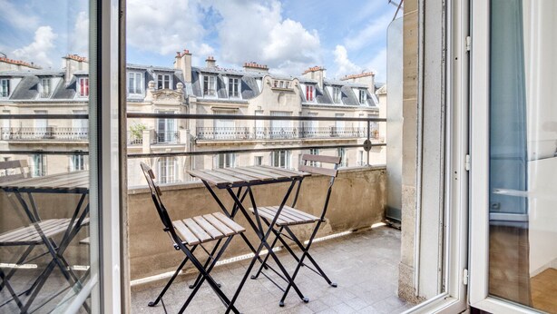 A balcony with a table and chairs, overlooking a row of traditional European-style buildings. - Blueground | La Muette, elev & balcony, nr mall (Paris)
