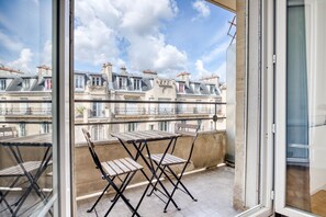 Un balcon avec une table et des chaises, donnant sur une rangée de bâtiments de style européen traditionnel.
