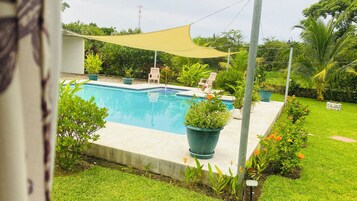 Una piscina rectangular con un deck perimetral, plantas en macetas y una zona con sombra.
