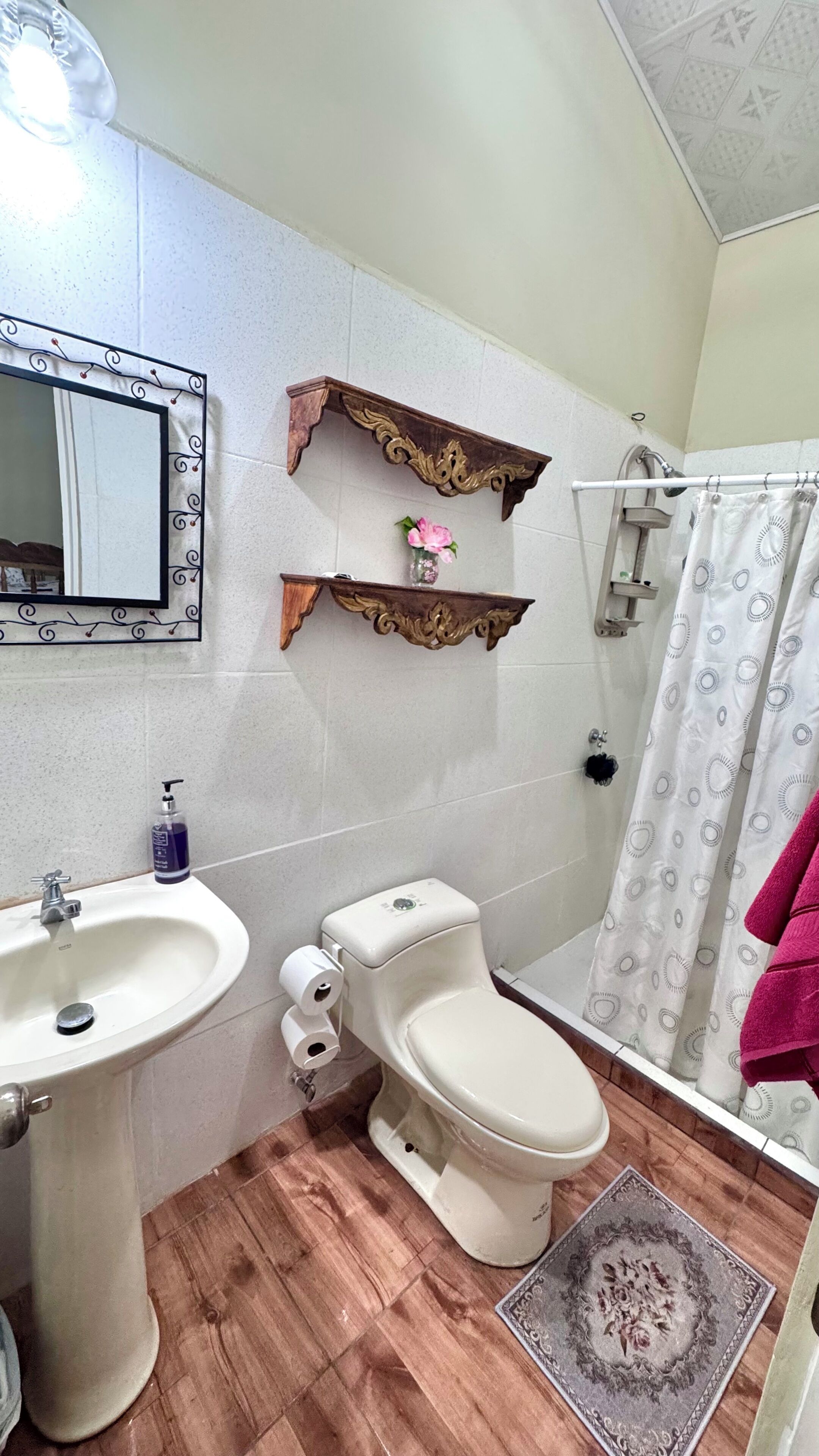 Een badkamer met een wastafel, toilet, douche, decoratieve spiegel en twee houten plankjes.