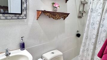 Een badkamer met een wastafel, toilet, douche, decoratieve spiegel en twee houten plankjes.