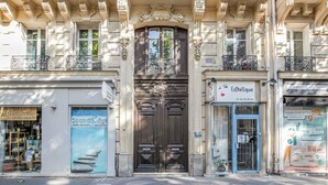 Une façade d’immeuble ornée de détails architecturaux, une porte d’entrée centrale et des devantures de magasins, notamment un salon de beauté et un commerce.
