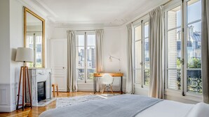 Une chambre à coucher avec un grand lit, un bureau, une chaise, une lampe et une cheminée.