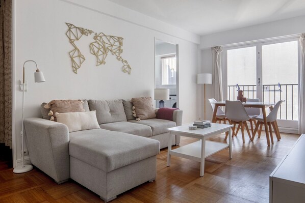 A modern living room with a grey sofa, a white coffee table, and a dining area with a table and chairs.