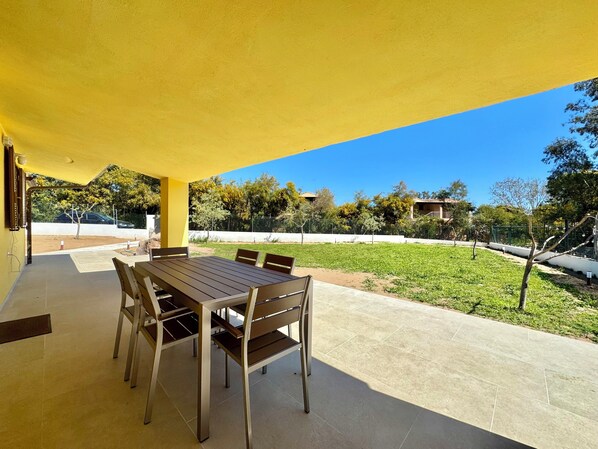 A covered patio with a table and chairs, a view of a grassy area, and a clear blue sky.