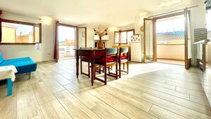 A spacious living area with a dining table, chairs, and a sofa. There is a balcony with a view of the city.